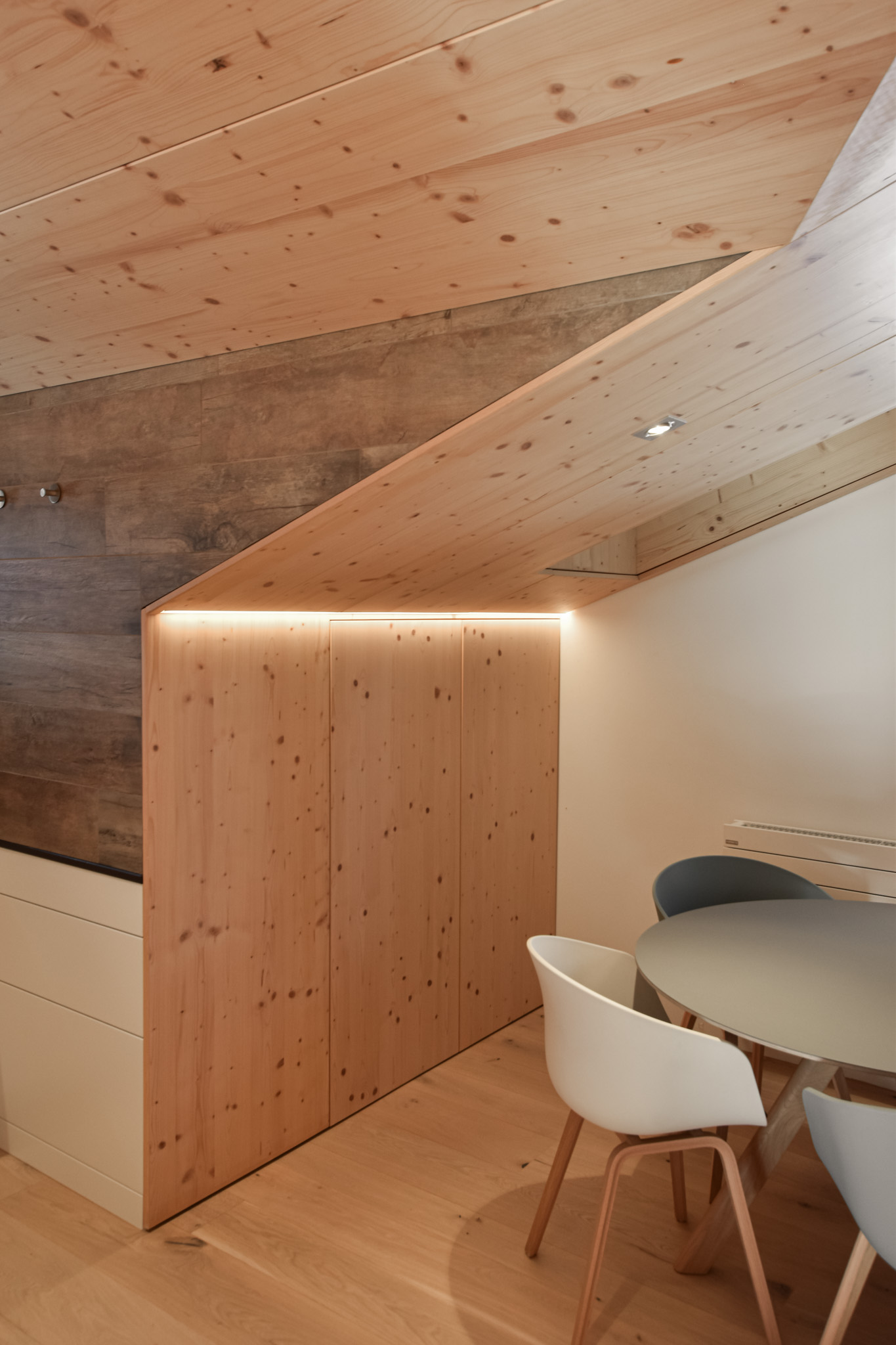A cozy, modern interior featuring wooden walls, a rounded table with chairs, and warm ambient lighting highlighting wood textures.