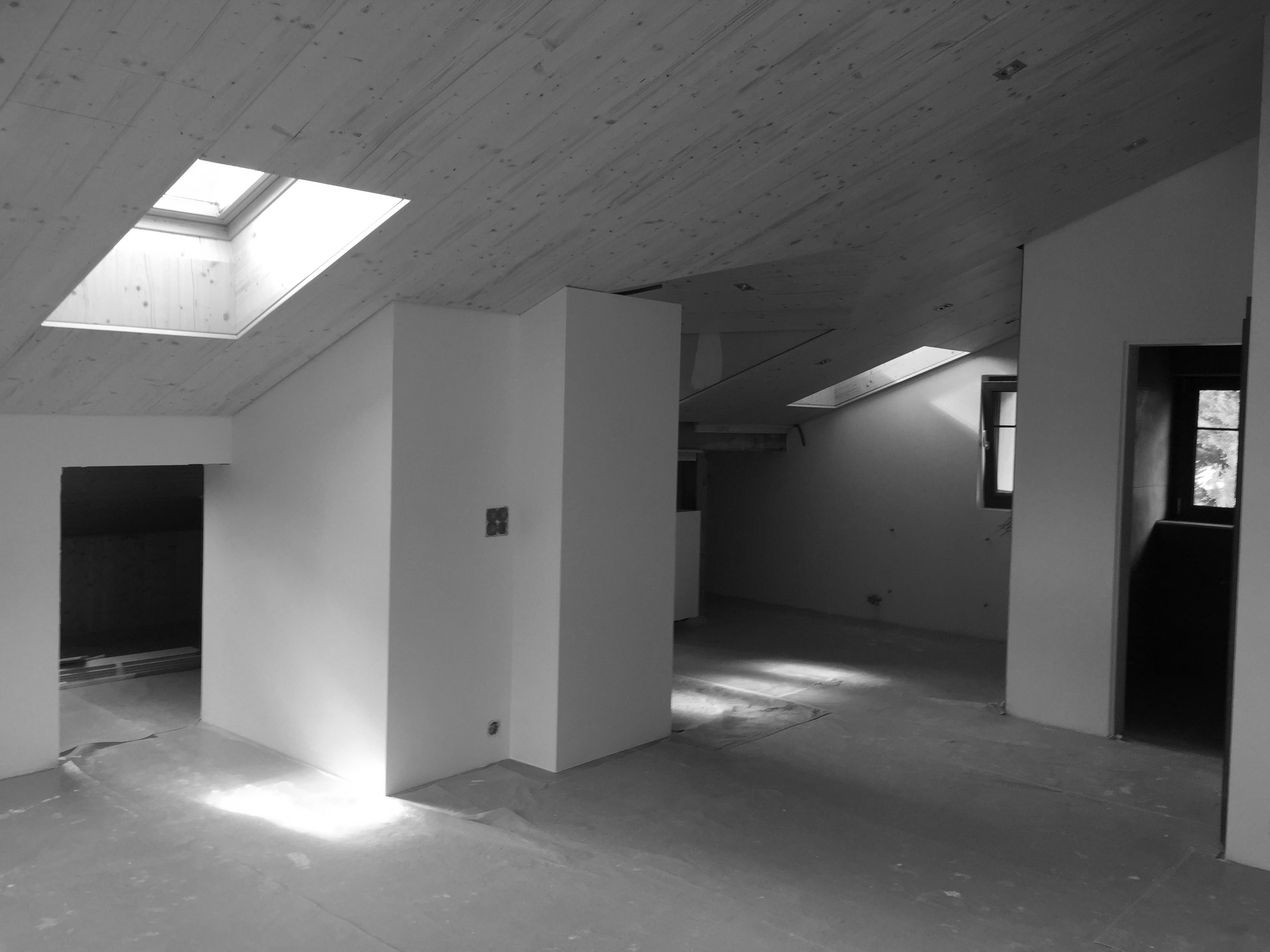 Light-filled attic interior with wooden ceiling, unfinished walls, and skylights casting soft shadows on the floor.