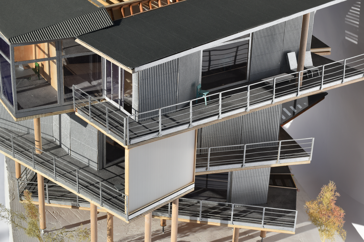 Detailed architectural scale model of a modern residential building featuring timber construction with corrugated metal cladding and multiple balconies, showcasing intricate building materials and construction details.