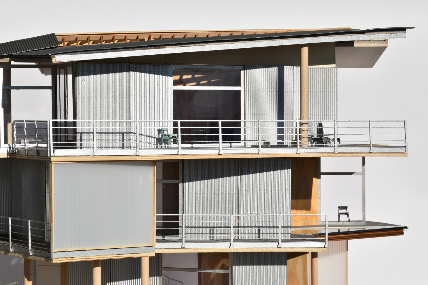 Detailed architectural scale model of a timber construction, featuring corrugated cladding, balconies, and a visible wood structure, emphasizing the intricate design and material choices.