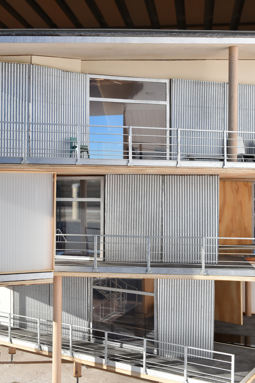 Architectural model of a three-story modern residential building, featuring a contemporary design with corrugated metal cladding and prominent wooden elements.