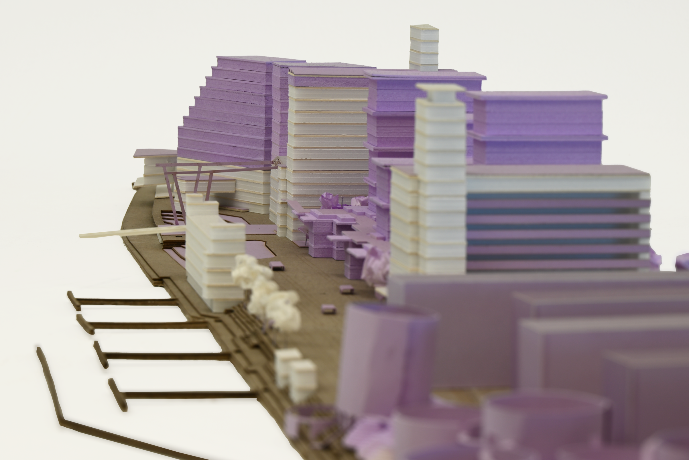 Architectural model in white foam, cardboard, and paper, with prominent purple elements highlighting key new buildings or landscape features in the project.